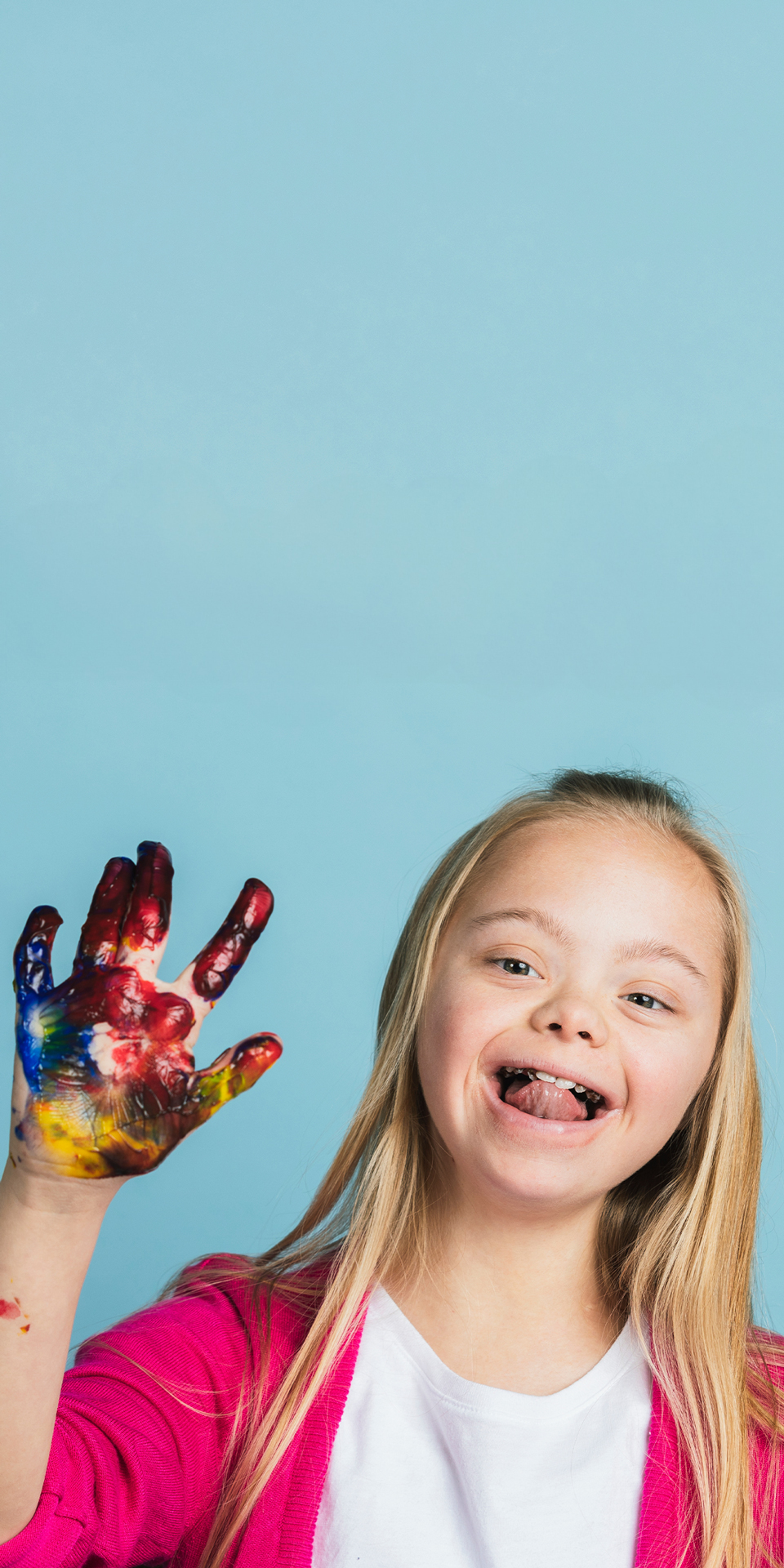 Image for Health and Human Services Category: young girl with Downs Syndrome smiling while holding up her hand which is covered in finger paints